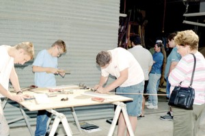 Grandmother Verla Horton looks on as Wathen students Jared Grumling, Ethan Little and Chris Zukowski build a miniature wooden airplane wing rib.