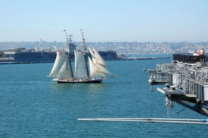 A vintage sailing ship passes between carriers Midway (foreground) and Abraham Lincoln (across the bay).