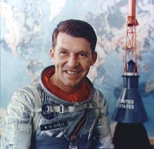 In a formal portrait from the 1960s, Wally Schirra, in his Mercury pressure suit, poses in front of a Mercury spacecraft model.